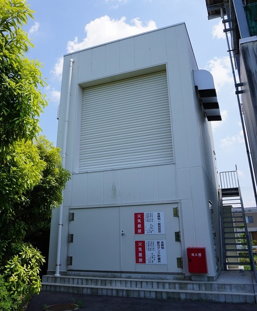 「火気厳禁」と書かれたプレートが貼られシャッターが閉まっている非常用発電機のための発電機棟を正面から写した写真