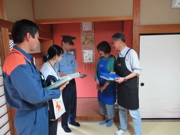 部屋の中で警察や消防、県薬事衛生課の三機関の方々が聞き取りを行っている様子の写真