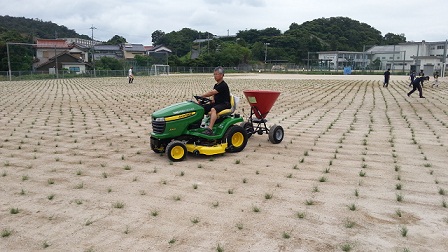 肥料散布機を使って芝生に肥料をまいている様子の写真