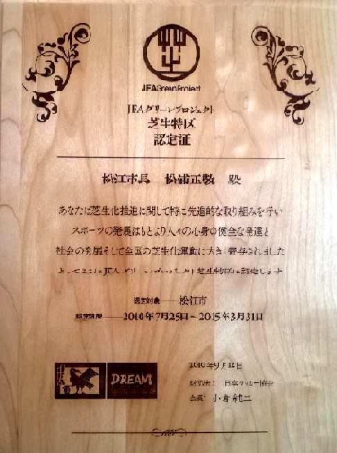 「あなたは芝生化推進に関して特に先進的な取り組みを行いスポーツの発展はもとより人々の心身の健全な発達と社会の発展そして芝生化運動に大きく寄与されました」と書かれている芝生特区認定証の写真