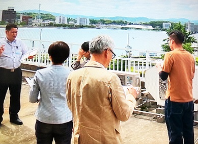海沿いの現庁舎の視察で、左側に立っている男性の話を参加者が聞いているワークショップの様子の写真