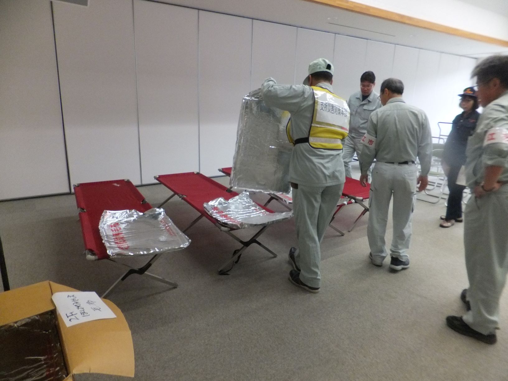 施設内で展開された簡易ベッド等の防災資機材と、それを点検する市職員たちの写真