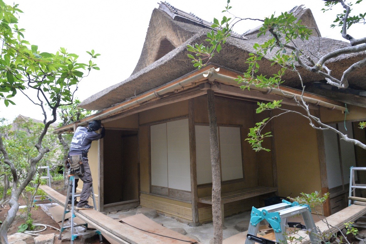 二つ割りにした竹を雨どいにして軒の下に設置している作業員の写真