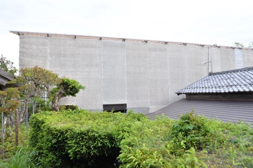 建物の周囲に組まれた足場に白いシートがかけられている写真
