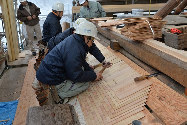 下屋庇の柿葺の木の板を打ち付けている作業員の写真