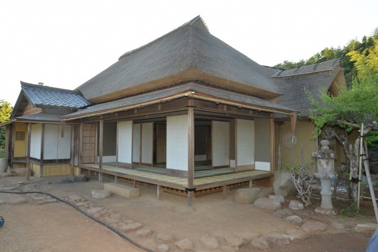 かやぶき屋根で障子の引き戸と縁側がある向月亭の建物と石灯籠や飛び石の道がある庭の写真