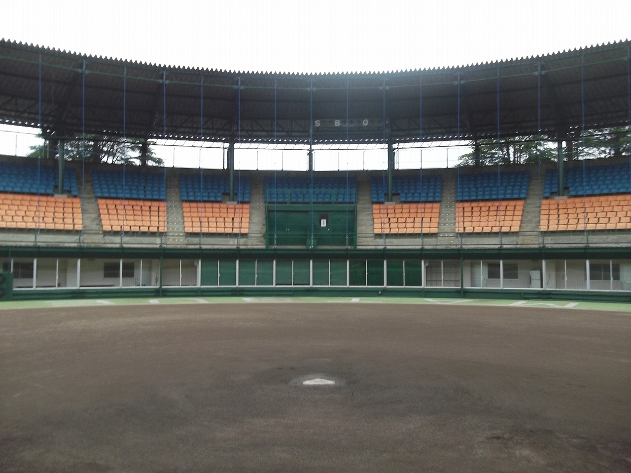 土でできた内野のマウンドからオレンジ色と青色の椅子を備えた観客席を撮影した写真