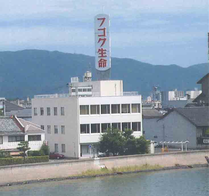 3階建ての白い建物の屋上に縦に赤文字でフコク生命と書かれた大きな看板が設置された富国生命保険相互会社の外観写真