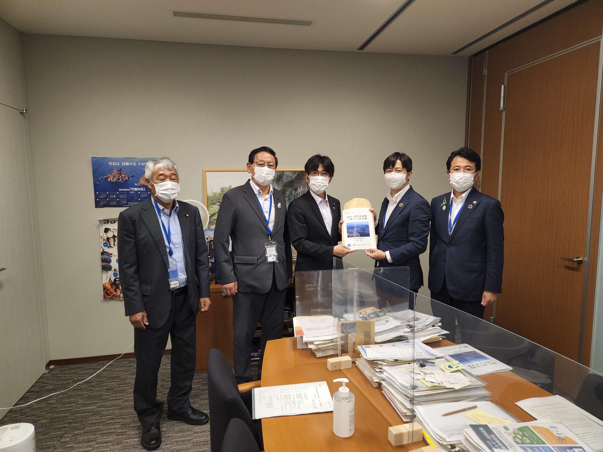 5名の男性が横一列に並び、中央に立つ舞立昇治参議院議員と同盟会の男性が一緒に要望書を持っている集合写真