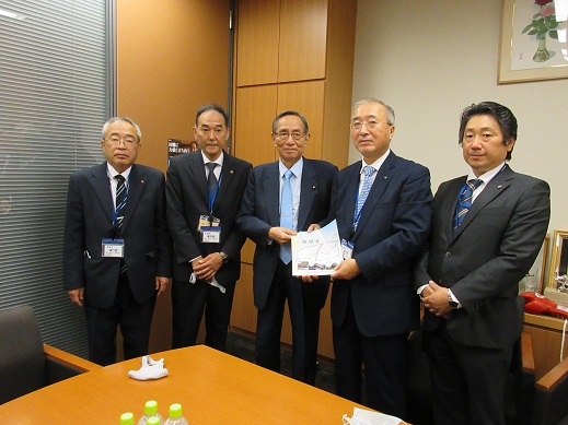 5名の男性が横一列に並び、中央に立つ細田博之衆議院議員と同盟会の男性が一緒に要望書を持っている集合写真