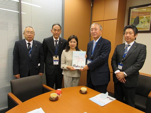 亀井亜紀子衆議院議員と4名の男性が横一列に並び、中央に立つ議員と同盟会の男性が一緒に要望書を持っている集合写真