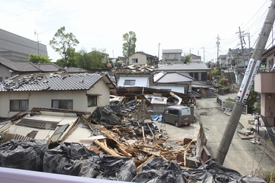 電柱は傾き、家の屋根瓦が剥がれ、家屋が傾いたり崩壊している災害被災地の写真
