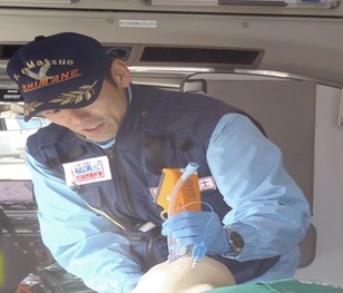 救急車の中で救急救命士の男性が器具使って気道確保を行っている写真