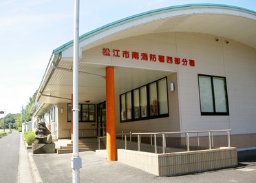 屋根が曲線造りで、入口上の壁に赤文字で「松江市南消防署西部分署」と書かれた建物外観の写真
