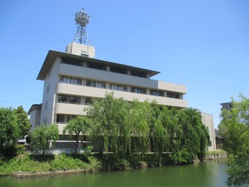 川が近くに流れている5階建ての消防本部庁の外観の写真