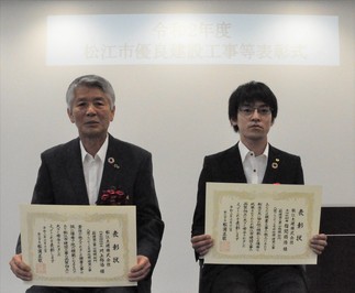 代表取締役社の長川上氏と主任技術者の福間氏が表彰状を手にして並んでいる写真