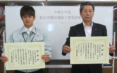 代表取締役の岡本氏と主任技術者の古瀬氏が表彰状を手にして並んでいる写真