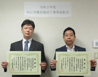 代表取締役社長の新田氏と主任技術者の曽田氏が表彰状を手にして並んでいる写真
