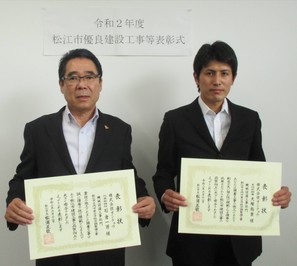 代表取締役の石倉氏と主任技術者の大塚氏が表彰状を手にして並んでいる写真