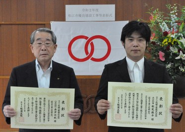 代表取締役の金津氏と主任技術者の松尾氏が表彰状を手にして並んでいる写真