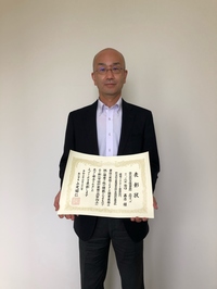 石本建築設計事務所の大阪オフィス代表の谷口氏が表彰状を手にして正面に向けている写真