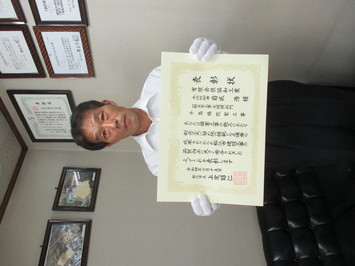 表彰状を持って正面に向けている有限会社協和工業の岩成浩氏の写真