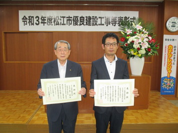 代表取締役の金津氏と主任技術者の小林氏が表彰状を手にして並んでいる写真
