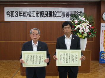 代表取締役の金津氏と主任技術者の岩崎氏が表彰状を手にして並んでいる写真