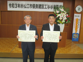 代表取締役の金津氏と主任技術者の三原氏が表彰状を手にして並んでいる写真