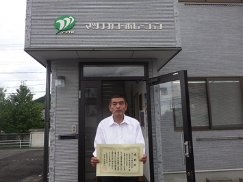 代表取締役・主任技術者の松近氏が表彰状を手にしている写真