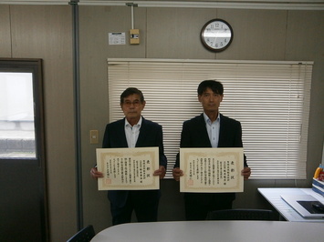 代表取締役の松本氏と主任技術者の松本氏が表彰状を手にして並んでいる写真