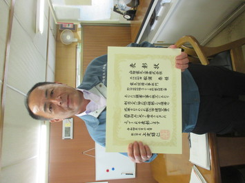 表彰状を持って正面に向けている山陰電気工事株式会社の松浦泰氏の写真