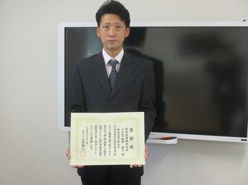 表彰状を持って正面に向けている松栄設備株式会社の松崎康介氏の写真