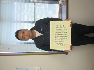 表彰状を持って正面に向けている有限会社キョウワビルト工業の中川一政氏の写真