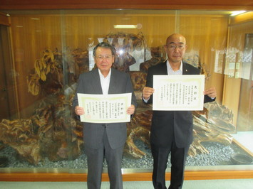 代表取締役の藤岡氏と主任技術者の原氏が表彰状を手にして並んでいる写真