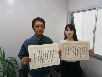 代表取締役の山本氏と主任技術者の槇原氏が表彰状を手にして並んでいる写真
