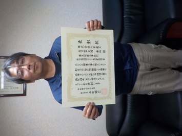 表彰状を持って正面に向けている株式会社八束電工の大西秀和氏の写真