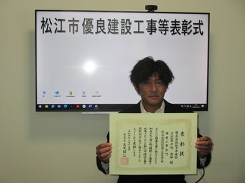 表彰状を持って正面に向けている株式会社佐々木建設の戸谷吉伸氏の写真