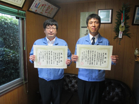 代表取締役の山代氏と主任技術者の豊島氏が表彰状を手にして並んでいる写真
