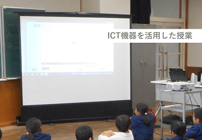 教室の黒板前に設置された、大型スクリーンや投影機等のICT機器群の写真