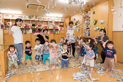 託児所の屋内で千切れ紙を飛ばして遊ぶ子どもたちの写真