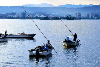湖面に浮かぶ4艘の小舟と、湖の向こう岸の嫁ヶ島および松江市市街地を望む遠景写真
