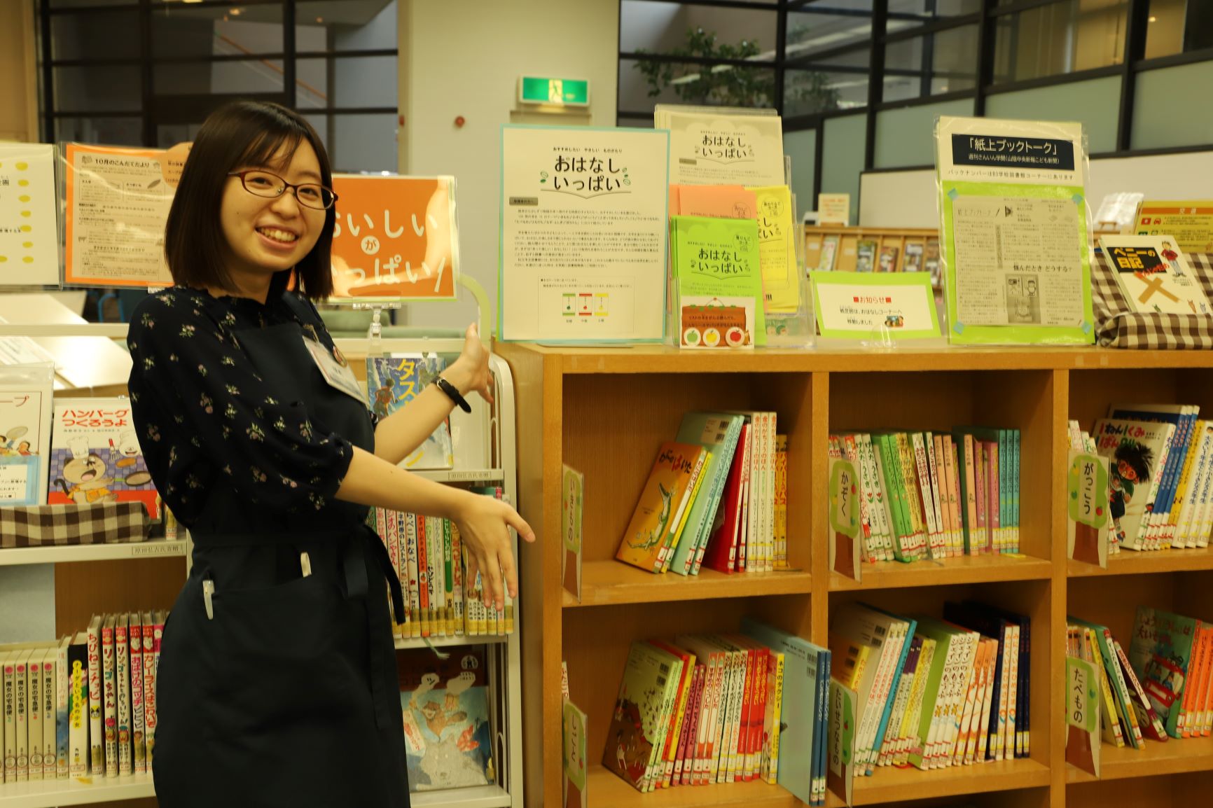 松江市立中央図書館館内に設けられたこども読書コーナーと、コーナーを紹介する女性職員の写真
