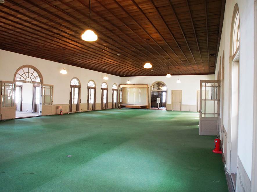 床は緑色の絨毯が敷かれ、天井に吊り下げ型の照明が設置されている興雲閣2階大広間の写真