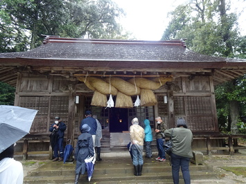 本殿の入り口上部に巨大なしめ縄が飾られている忌部神社で参拝している参加者の写真