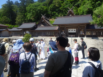 階段の先にある佐太神社の本殿と権禰宜さんの話を聞いている参加者の写真