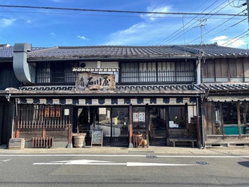 建物中央の屋根に「石川屋」と書かれた看板が設置され、通りに面して木製格子が施されている2階建ての建物外観の写真