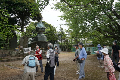 公園内の石碑の前で説明しているガイドの男性と話を聞いている参加者の写真