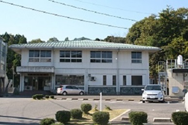 青空の下、鹿島武道館の施設外観正面の写真、建物前の駐車場に車が2台駐車している