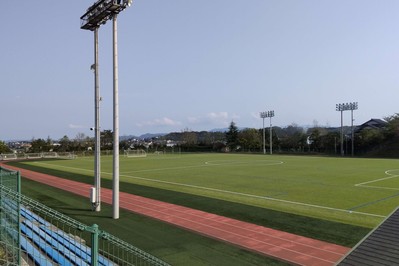 青い空を背景に、中央に芝生の生えたサッカーフィールドとその周囲を囲む赤い3レーンの競走用トラックのある競技場を、斜めから撮影した写真